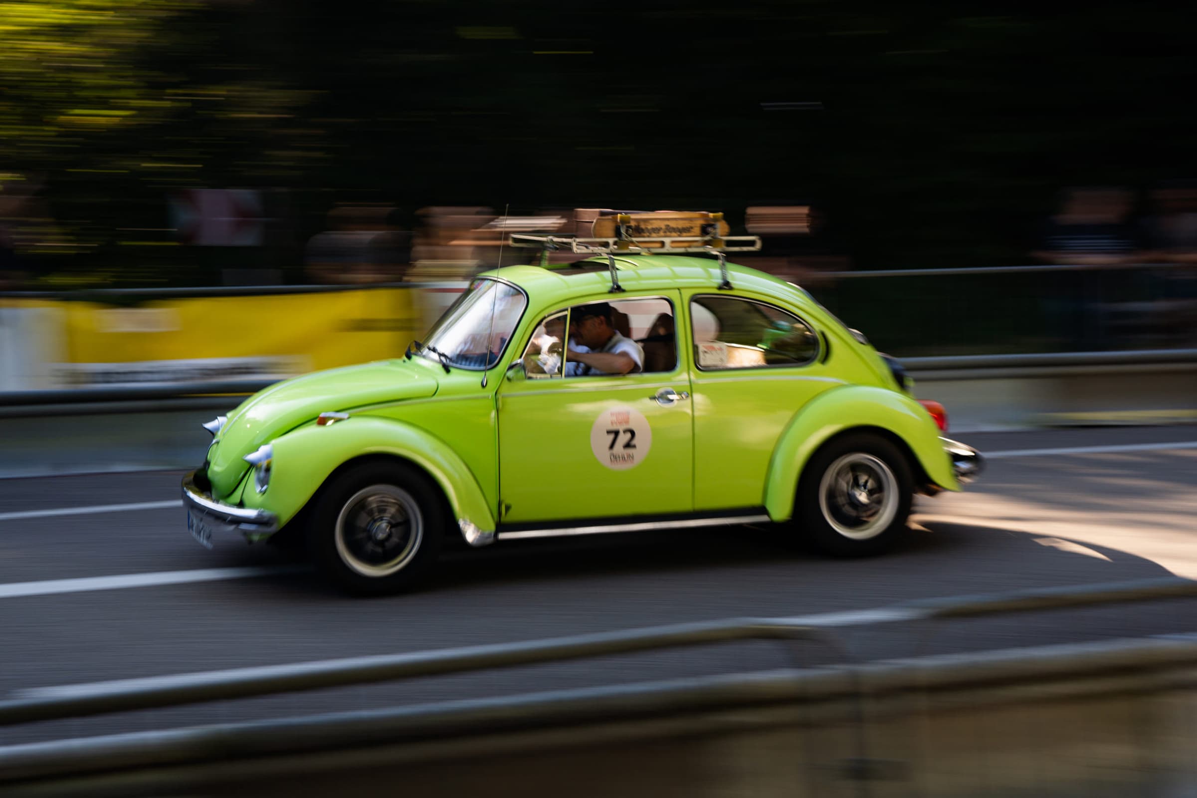 Lime-green classic beetle with a roof rack racing past spectators, panned with motion blur