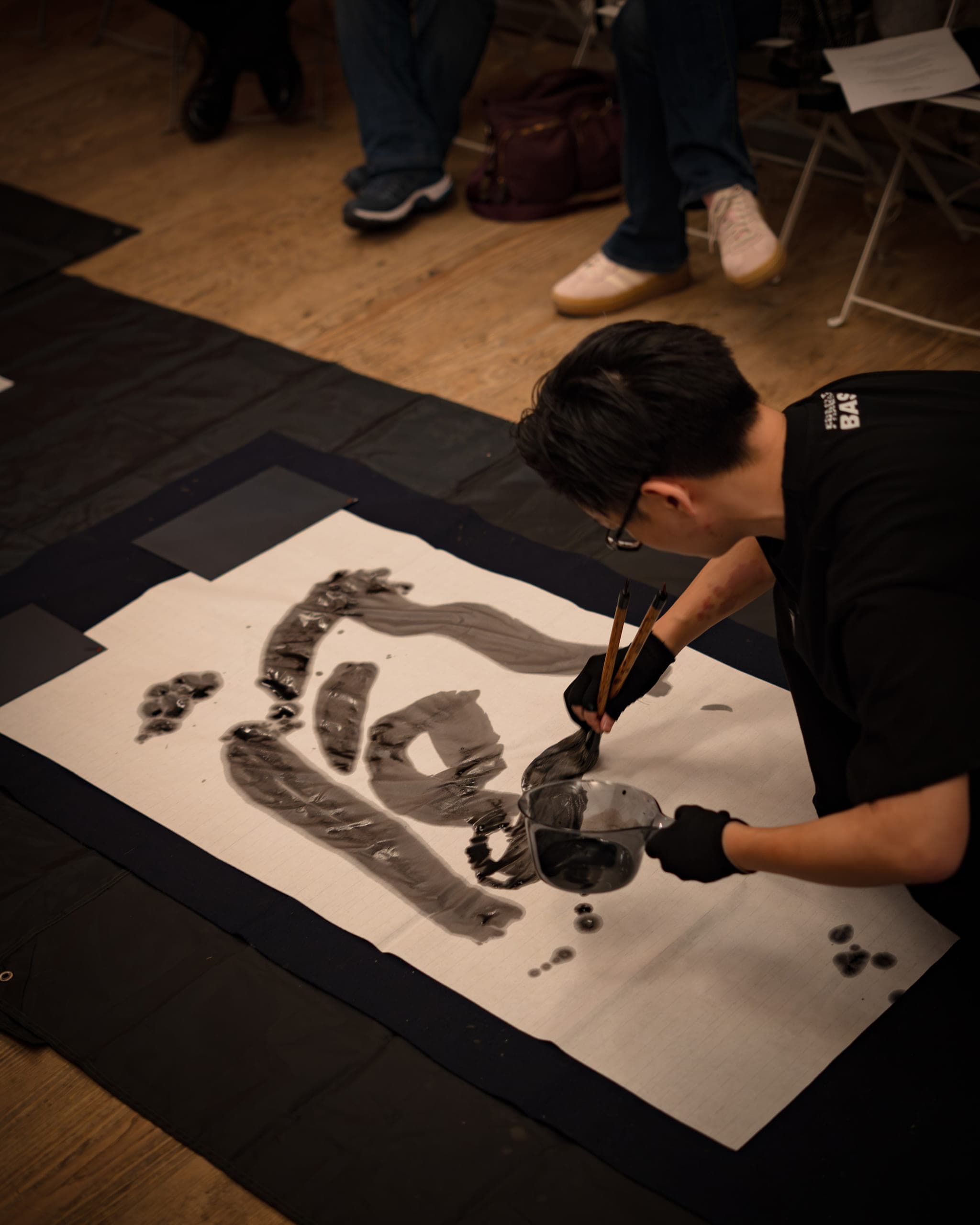 Calligrapher in gloves painting large ink strokes on a sheet of paper on the floor