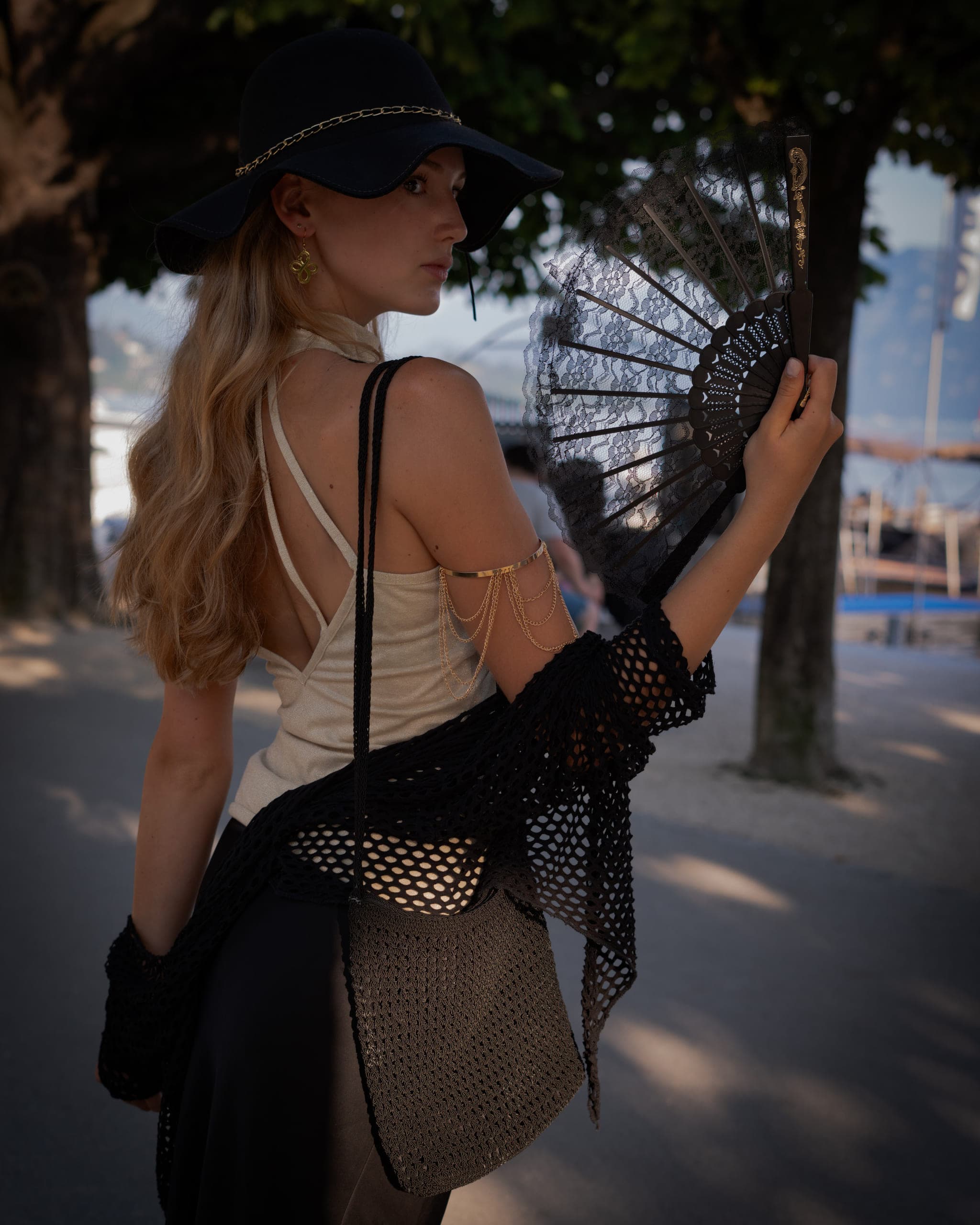 Woman in a wide-brimmed hat holding a black lace fan, looking over her shoulder in warm evening light